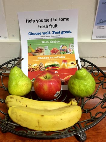 A bowl of fruit with a sign to help yourself